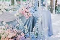 a beautiful blue and pink wedding tablescape with a blue tablecloth, lush florals and a light curtain behind is amazing