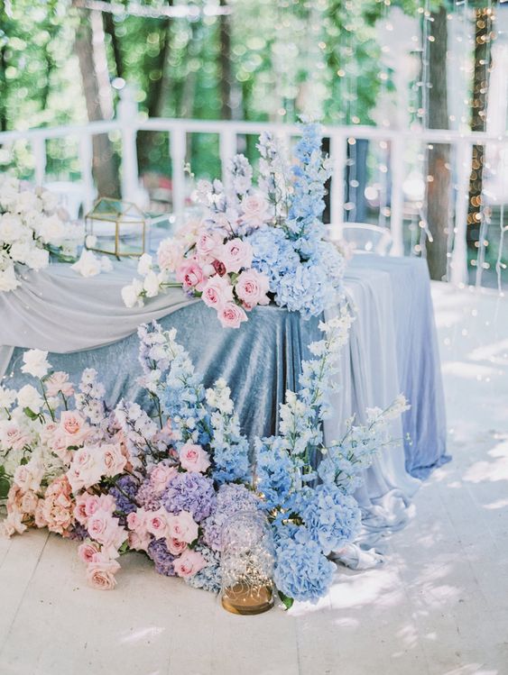 a beautiful blue and pink wedding tablescape with a blue tablecloth, lush florals and a light curtain behind is amazing