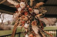 a beautiful boho fall wedding arch decorated with blush, rust blooms, eucalyptus, pampas grass and dried touches here and there