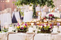 a beautiful indoor secret garden wedding tablescape with neutral linens and cool menus, with bold bloom centerpieces and an additional hanging one