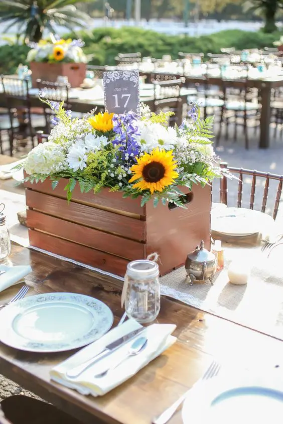 a beautiful rustic wedding centerpiece in a crate, with sunflowers, white hydrangeas, purple blooms, baby's breath and fern is a gorgeous solution