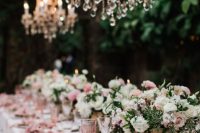 a beautiful secret garden wedding tablescape with white and blush blooms and greenery, pink linens, pink glasses and crystal chandeliers
