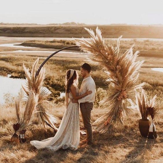 a boho fall round wedding arch with pampas grass, bold dried blooms and leaves plus pampas grass in vases around