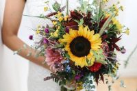 a bold boho fall wedding bouquet of purple, pink and blue flowers, large sunflowers, greenery and berries is a cool idea for fall