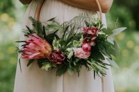 a bold hoop wedding bouquet with lots of greenery, pink blooms and a large king protea is a cool idea for a modern and romantic bride