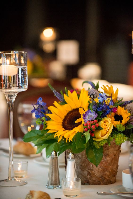 a bold wedding centerpiece with sunflowers, yellow roses, purple and blue flowers, astilbe and foliage is a fantastic idea