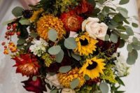 a bright cascading wedding bouquet of sunflowers, red and yellow dahlias, white and burgundy roses, greenery and berries