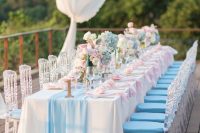 a bright glam wedding tablescape with a blue table runner and napkins, blue, pink and white blooms, blue candles and gold touches