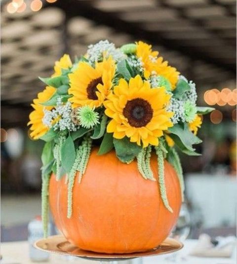 a bright summer wedding centerpiece of sunflowers, greenery and baby's breath placed into a pumpkin is perfect for a bold fall wedding