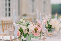 a chic pastel wedding tablescape with neutral and pink blooms and greenery, blue candles, pink glasses and a blush tablecloth