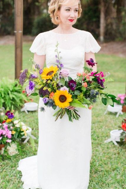 a colorful and sumptuous wedding bouquet with purple and deep purple blooms, fuchsia, pale pink touches, various greenery and sunflowers