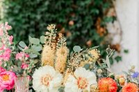 a colorful secret garden wedding tablescape with a greenery and colorful bloom runner, colorful glasses, layered plates and gold cutlery