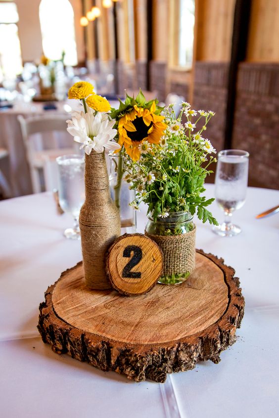 a cool rustic wedding centerpiece of sunflowers, daisies, gerberas, burlap and rope plus a wood slice is a lovely solution for summer