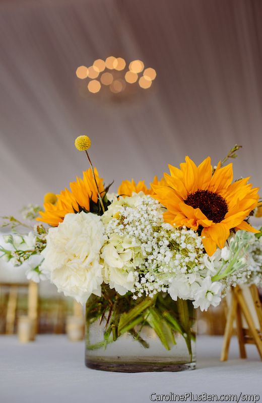 a cool wedding centerpiece with white roses, sunflowers, baby's breath and billy balls is a lovely and cute arrangement for a rustic wedding