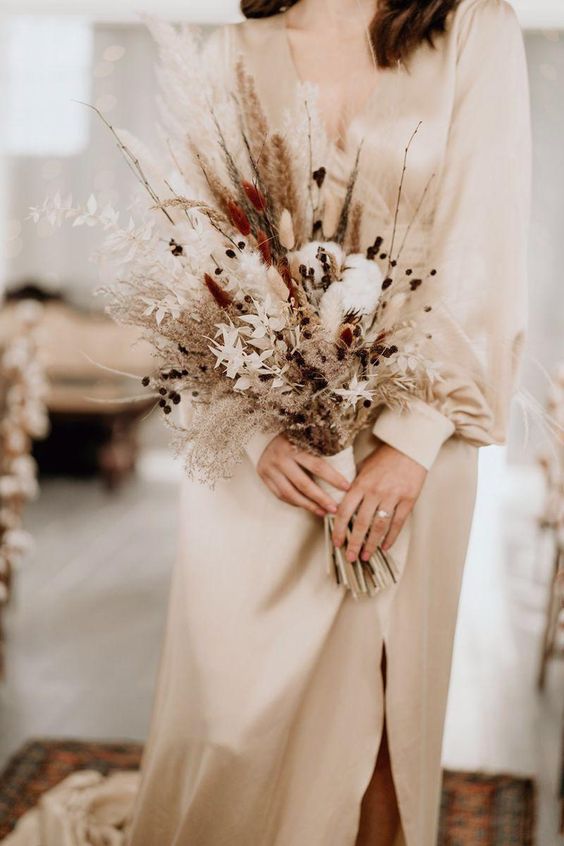 a delicate dried wedding bouquet of cotton, bunny tails, berries, twigs, dried foliage and grasses plus ribbons is ideal for fall