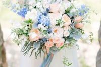 a delicate wedding bouquet of blush roses, peonies, blue delphinium, greenery and long matching ribbons is amazing