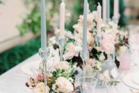 a delicate wedding tablescape with blue and blush candles, pink glasses, neutral and dark blooms and greenery plus gold cutlery