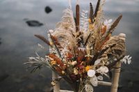 a dried fall wedding bouquet with lunaria, astilbe, feathers, proteas, daises and bunny tails, grasses and greenery for a fall boho wedding