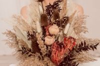 a dried flower wedding bouquet with dried peonies, astilbe and thistles, king proteas, fronds, dark foliage and grasses is a cool idea for the fall