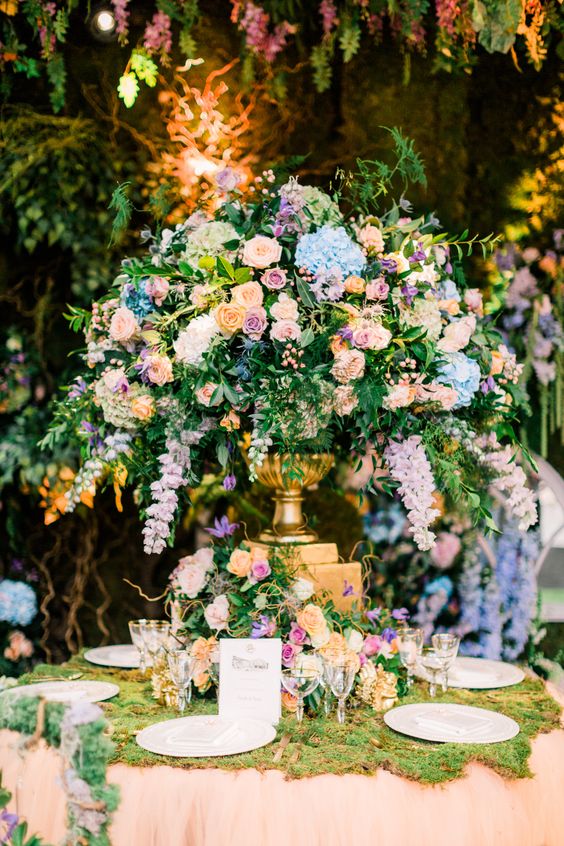 a fabulous garden wedding tablescape with a lush pastel floral centerpiece on a stand, a moss runner and gold edge glasses is amazing