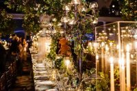 a fantastic indoor secret garden wedding tablescape with lots of greenery, candle lanterns and candelabras, elegant curlery and white plates