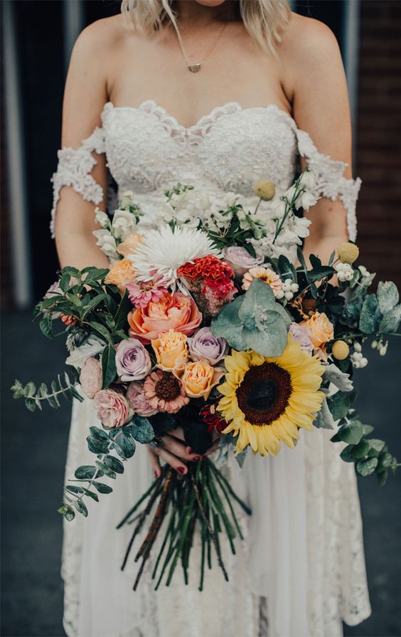 a gorgeous and colorful wedding bouquet of yellow and lilac roses, red and pink blooms, sunflowers, billy balls, white flowers and greenery