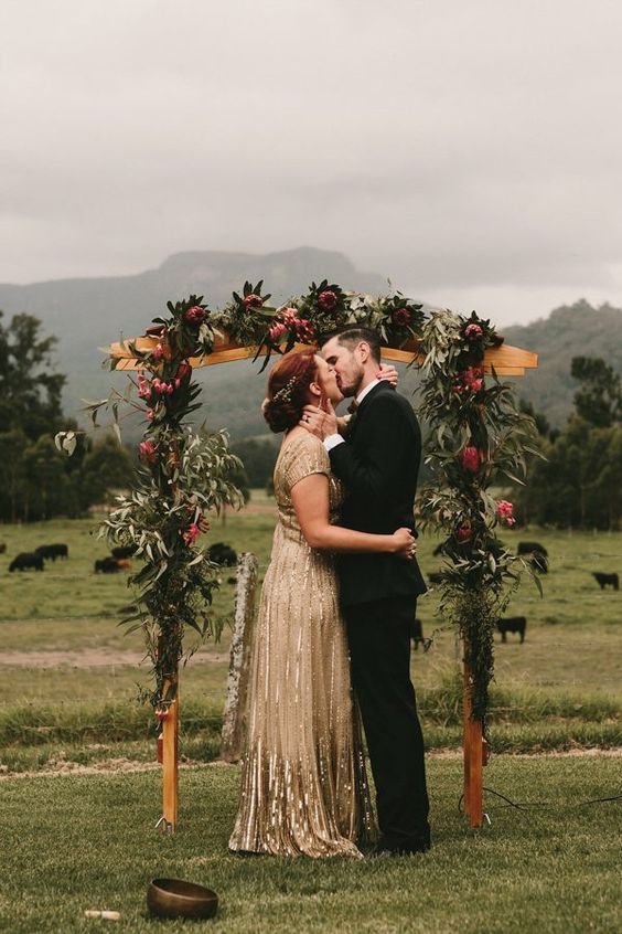a gorgeous rustic fall wedding arch with greenery, pink king proteas, deep purple blooms is a very stylish and elegant idea