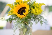 a lovely and simple rustic wedding centerpiece of a wood slice, horseshoes, a jar with eucalyptus, mimosas and sunflowers is a bright idea