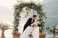 a lovely wedding arch made of greenery, pink, white and blue flowers and matching arrangements around is a gorgeous idea