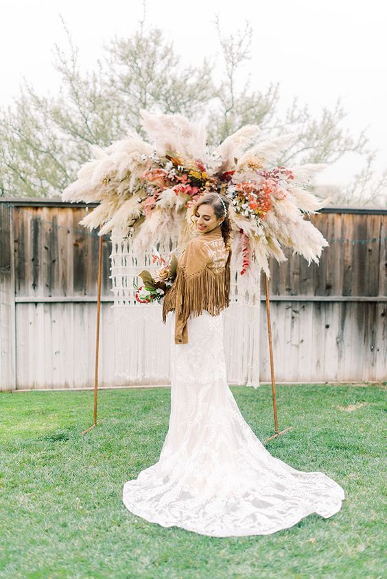 a lush and bold boho fall wedding arch with pampas grass and bold blooms plus macrame hanging down is amazing