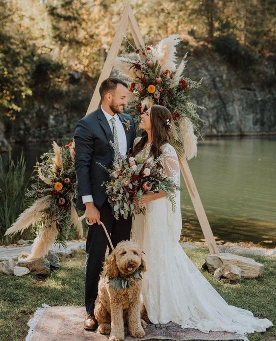 a lush triangle boho fall wedding arch with greenery, pampas grass, pink, orange and burgundy blooms is very cool
