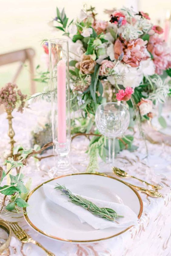 a magical garden wedding tablescape in pink shades, with a lush floral centerpiece, pink candles, a printed tablecloth and greenery