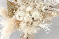 a neutral dried flower wedding bouquet with ferns, daisies, fronds, bunny tails, seed pods and pampas grass plus tan ribbons