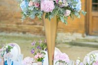 a pastel wedding tablescape with blue and pink vases, blush plates, tall pink and blue floral centerpieces and gold cutlery and chargers
