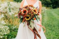 a pretty and bold fall wedding bouquet of sunflowers, roses, greenery, feathers and with long and bold ribbons is wow
