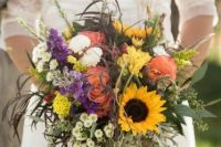 a pretty and colorful summer wedding bouquet with much textural greenery, sunflowers, pink, purple and yellow blooms is a lovely idea