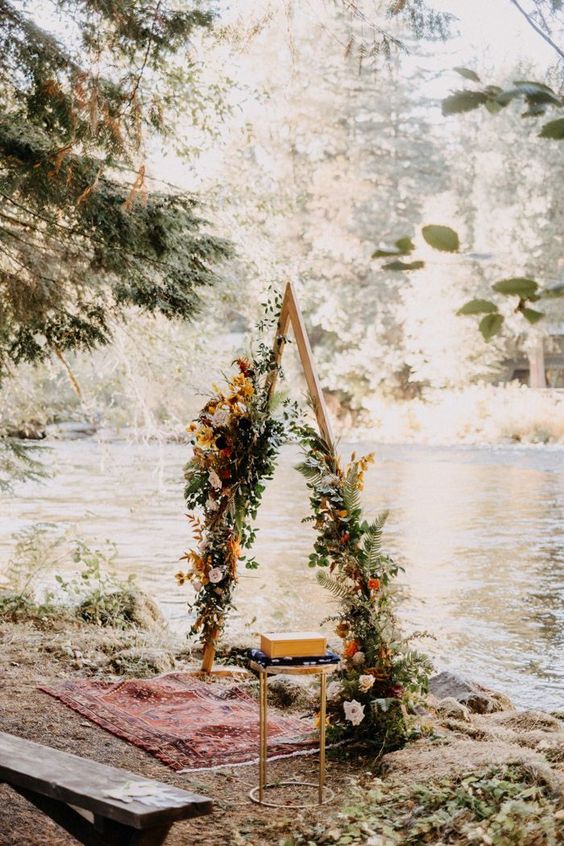a pretty boho fall triangle wedding arch done with greenery, rust, blush and pink blooms, dried grasses and leaves