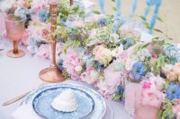 a pretty pink and blue wedding tablescape with a pink tablecloth, a pink and blue floral runner, pink candles and glasses, pink printed plates