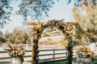 a pretty rustic fall wedding arch with greenery, white and burgundy blooms, pampas grass and matching arrangements at the base