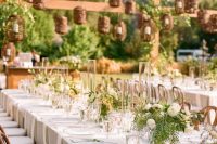 a pretty secret garden wedding tablescape with neutral linens, greenery and white blooms, candle lanterns hanging over the space