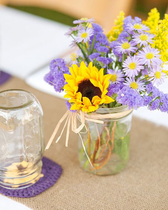 a pretty wedding centerpiece of lilac blooms and sunflowers plus mimosas is a very cool idea for a bright summer wedding