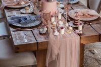 a pretty wedding tablescape with a pink tulle runner, pink blooms in a pot, a pink wedding cake, pink and blue napkins and lots of desserts