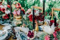 a refined secret garden wedding table setting with a blue table runner and floral plates, bold blooms and greenery, black candles and chic glasses
