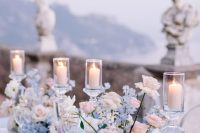 a refined wedding tablescape with a blue tablecloth, blush, blue and lilac blooms, candles and clear chargers and glasses