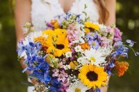 a relaxed and colorful wildflower wedding bouquet with sunflowers, daisies, blue and pink blooms and baby’s breath