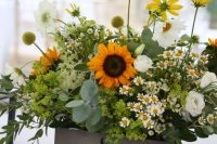 a relaxed rustic wedding centerpiece in a crate, with sunflowers, daisies, greenery, billy balls, green hydrangeas and white ranunculus is wow
