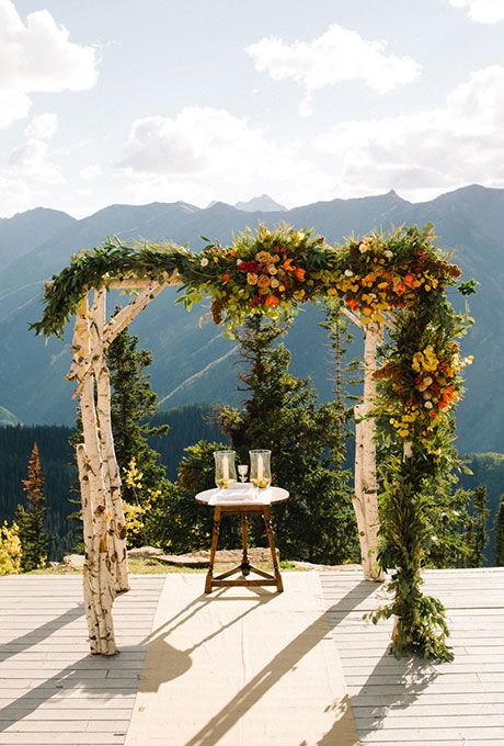 a rustic fall wedding arch of birch branches with lush greenery and super bright blooms is a bold and cool option