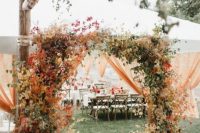 a rustic wedding arch covered with bright fall leaves and greenery plus candles around is a cool idea for fall