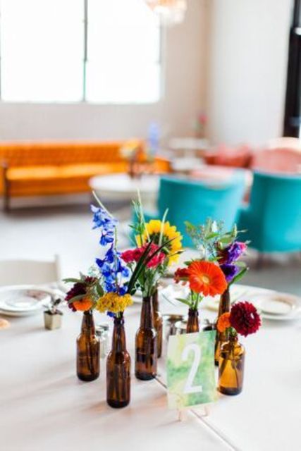 a simple cluster wedding centerpiece of beer bottles with lots of colorful blooms and a marble table number is a cool idea