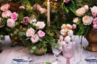 a sophisticated secret garden wedding table setting with greenery and pink rose centerpieces, printed plates, blush glasses and a tablecloth